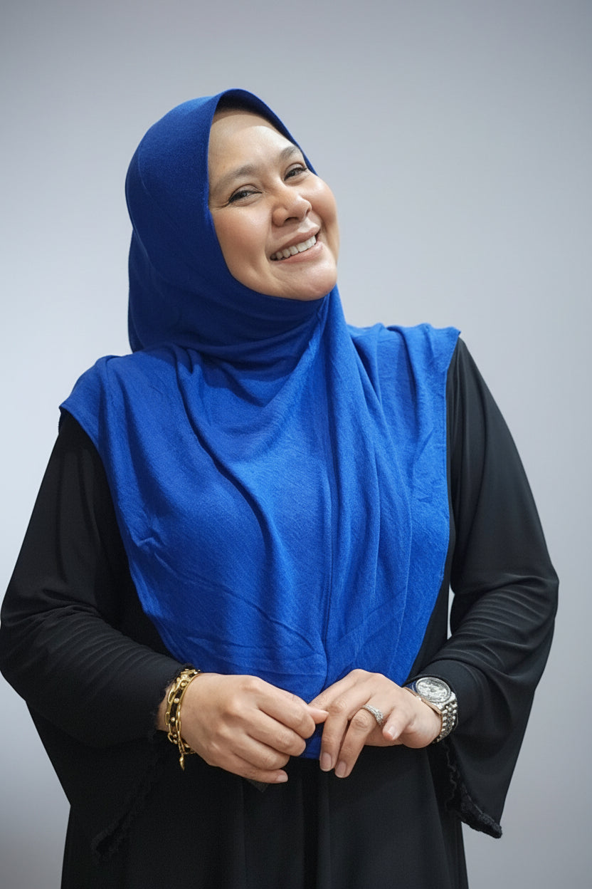 A smiling woman wearing a bright royal blue Tudung Daisy Munawwarah and a black long-sleeve dress